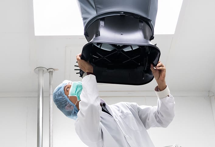 Technician in white overall and with face mask putting a funnel over a ceiling duct grill
