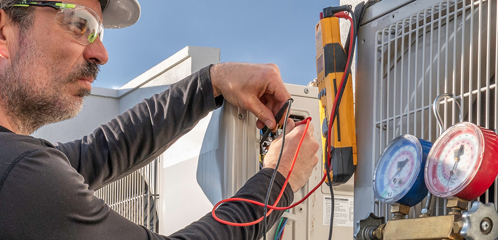 Technician shown measuring electrical currents on an air conditioning unit